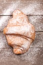 Croissant sprinkled with powdered sugar on old wooden board Top view