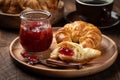 Croissant with strawberry preserves on wooden plate