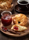 Croissant with strawberry preserves on wooden plate