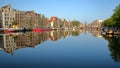 Crooked and colorful heritage buildings and houseboats, overlooking Amstel river with perfect reflections