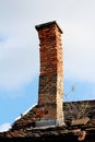 Crooked leaning old chimney made of dilapidated cracked red bricks with concrete cap on top built on roof of abandoned family Royalty Free Stock Photo