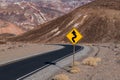 A crooked road sign along a highway curving through a barren and rugged desert landscape Royalty Free Stock Photo