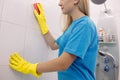 Crop of blonde woman from cleaning company cleaning wall in white bathroom. Royalty Free Stock Photo