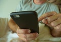 Crop face portrait with close up hands holding mobile phone of young man at home bedroom using internet social media app on smartp Royalty Free Stock Photo