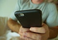 Crop face portrait with close up hands holding mobile phone of young man at home bedroom using internet social media app on smartp Royalty Free Stock Photo