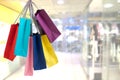 Crop female hand holding colorful paper bags on background of shopping center.