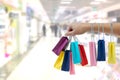 Crop female hand holding colorful paper bags on background of shopping center.