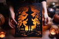 Halloween postcard with silhouette of paper witch in female hands on table among pumpkins and candles