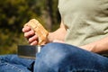 Crop female with delicious bread in hand sitting against blurred forest