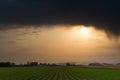 Crop field at sunset on a cloudy day. Big heavy clouds can be seen at the top and the sun rays coming up Royalty Free Stock Photo