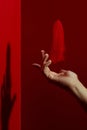 Crop hand gentle hand levitating feather against red background