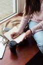 Crop girl with coffee writing in notepad