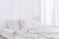 Crop image of white bed on the floor with pillows, blankets and lamp. White bedroom decoration with white curtain on the window