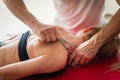 Crop masseuse doing massage with IASTM tool on shoulder of female client