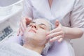 Crop master applying white mask with brush on face and neck of young woman in towel lying on table