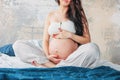 Crop photo of  beautiful pregnant girl young woman with long curly hair sitting in lotus pose on bed. Pregnancy yoga and nature Royalty Free Stock Photo