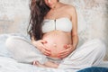 Crop photo of  beautiful pregnant girl young woman with long curly hair sitting in lotus pose on bed. Pregnancy yoga and nature Royalty Free Stock Photo