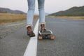 Crop photo of women`s legs in jeans on longboard on road with the mountains background