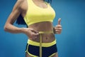 Crop shot of fitness woman in sport outfit measuring waistline with metric tape and showing thumb up. Good results of exercising