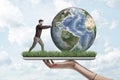 Crop side view of woman`s hand holding digital tablet with green grass growing on screen and little man pushing planet Royalty Free Stock Photo