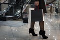 Crop of trendy woman on heels carrying black shopping paper bag while walking in shopping center. Young girl in black standing