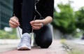 Crop unrecognizable woman runner wearing hygiene protective face mask sitting and tieing shoe rope during workout running in city Royalty Free Stock Photo