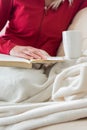 Crop view of young adult woman is relaxing on comfortable sofa with book and hot beverage