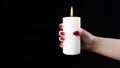 Crop woman with burning candle in studio. Crop female with red nails holding burning candle in hands against black