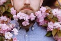 Croped photo of hipster Man and blooming pink cherry or sakura flowers in a beard. pink Flowers in a beard against the background