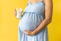 croped portrait cute pregnant unrecognizable woman in floral blue dress hold drink glass of milk on yellow background Royalty Free Stock Photo