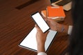 Croped shot of hand holdind smartphone and tablet with blank screen on wooden table.