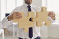 Cropped businessman or company manager in office wear joining two pieces of jigsaw puzzle