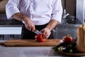 cropped chef man cutting fresh bell pepper using knife on wooden cutting board