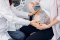 Cropped close up image of unrecognizable female doctor obstetrician, examining young pregnant woman sitting on couch in