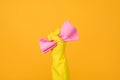 Cropped close-up photo of a hand in yellow glove holding a pink rubber for dusting isolated on yellow background. Housekeeping Royalty Free Stock Photo