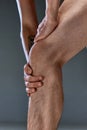 Cropped close up photo of leg of young athletics man touching knee at pain point. Male model posing shirtless Muscular Royalty Free Stock Photo