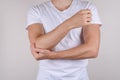 Cropped close up photo portrait of unhappy upset sad guy holding touching painful elbow wearing white t-shirt isolated grey backgr