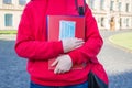 Cropped close up photo of smart clever teenager in casual red jumper holding notebooks and medical mask in hands