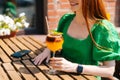 Cropped close-up shot of smiling young woman holding glass with cold exotic cocktail sitting at table in outdoor cafe in Royalty Free Stock Photo