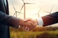 Cropped closeup of a handshake between two businessmen with a wind turbines background as concept of renewable energy Royalty Free Stock Photo