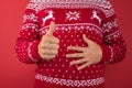 Cropped closeup photo of man in red and white christmas sweater holding his stomach and making thumb-up on isolated red background Royalty Free Stock Photo