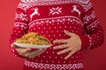 Cropped closeup photo of man in red and white christmas sweater holding large plate of food and touching his hurting stomach on Royalty Free Stock Photo