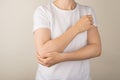 Cropped closeup photo of young woman in white t-shirt holding her right elbow on grey background