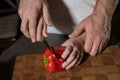 Cropped closeup portrait of father and kid's hands cutting red bell pepper in the kitchen with knife on wooden cutting boar
