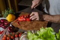 Cropped closeup portrait of male hands cutting red bell pepper in the kitchen with knife on wooden cutting board. Onion, pumpkin, Royalty Free Stock Photo