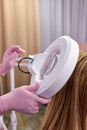 cropped doctor cosmetologist examines head skin of female patient with special dermatology equipment system