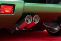 Cropped of double exhaust pipe and back part with tail light of modern green parked car. Waste gases release system of Royalty Free Stock Photo