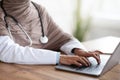 Cropped of female doctor using laptop, sitting in her cabinet Royalty Free Stock Photo