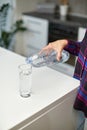 Closeup of a female hand holding drinking water bottle and pouring water into glass on table on kitchen background. Royalty Free Stock Photo