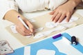 Cropped female seamstress draw contours with pen of pinned paper sew patterns on textile sheet on table. Toys, clothes